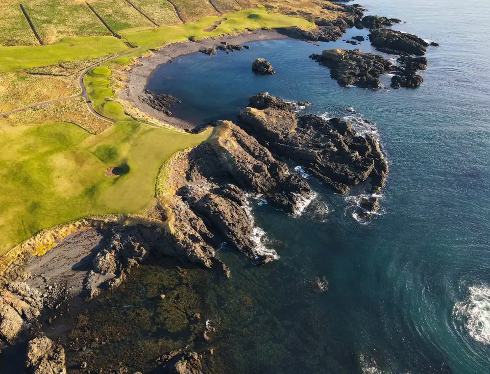 Horseshoe bay with black-sand beach and sea stacks beside the green